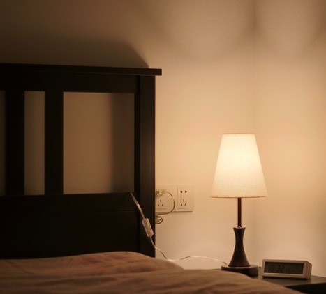 Lampka nocna z żarówką o barwie ciepłej na stoliku przy łóżku w sypialni