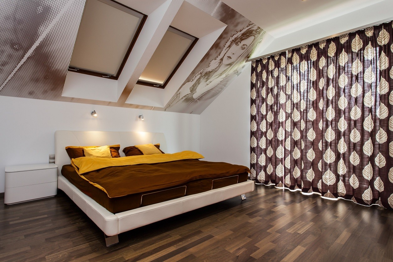 Sypialnia z ukośnym sufitem i kinkietami umieszczonymi za wezgłowiem łóżka