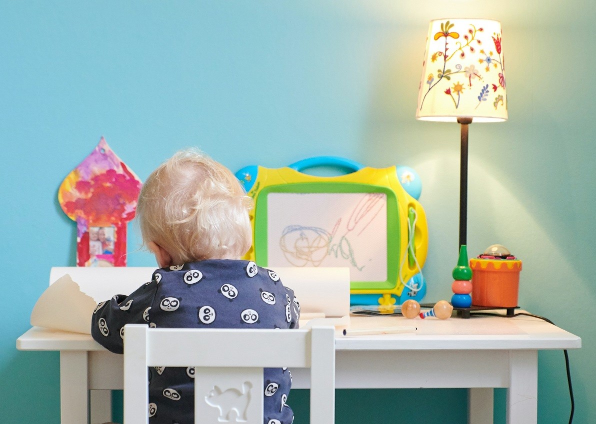 Chłopczyk rysujący przy biurku obok lampki biurkowej